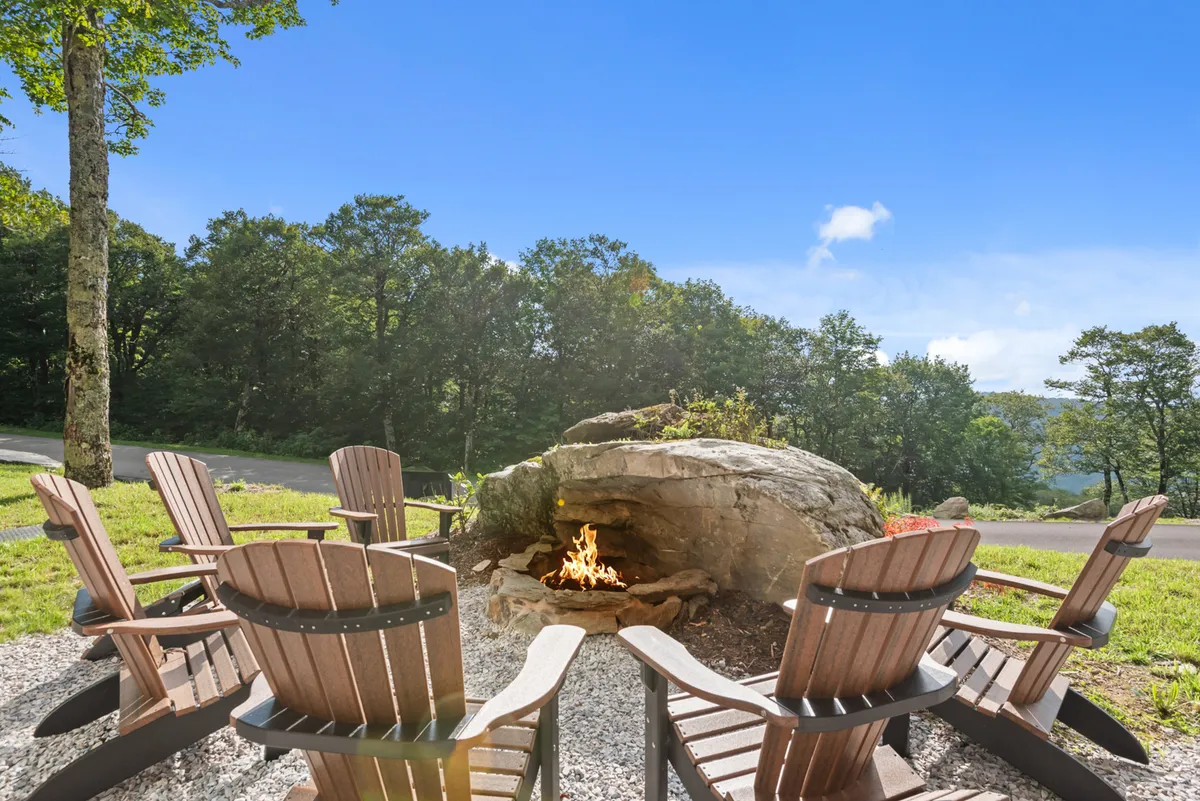 A cozy fire pit area encircled by Adirondack chairs, set among tall trees, inviting gatherings around a crackling fire. The environment is ideal for storytelling, roasting marshmallows, and stargazing under the night sky.