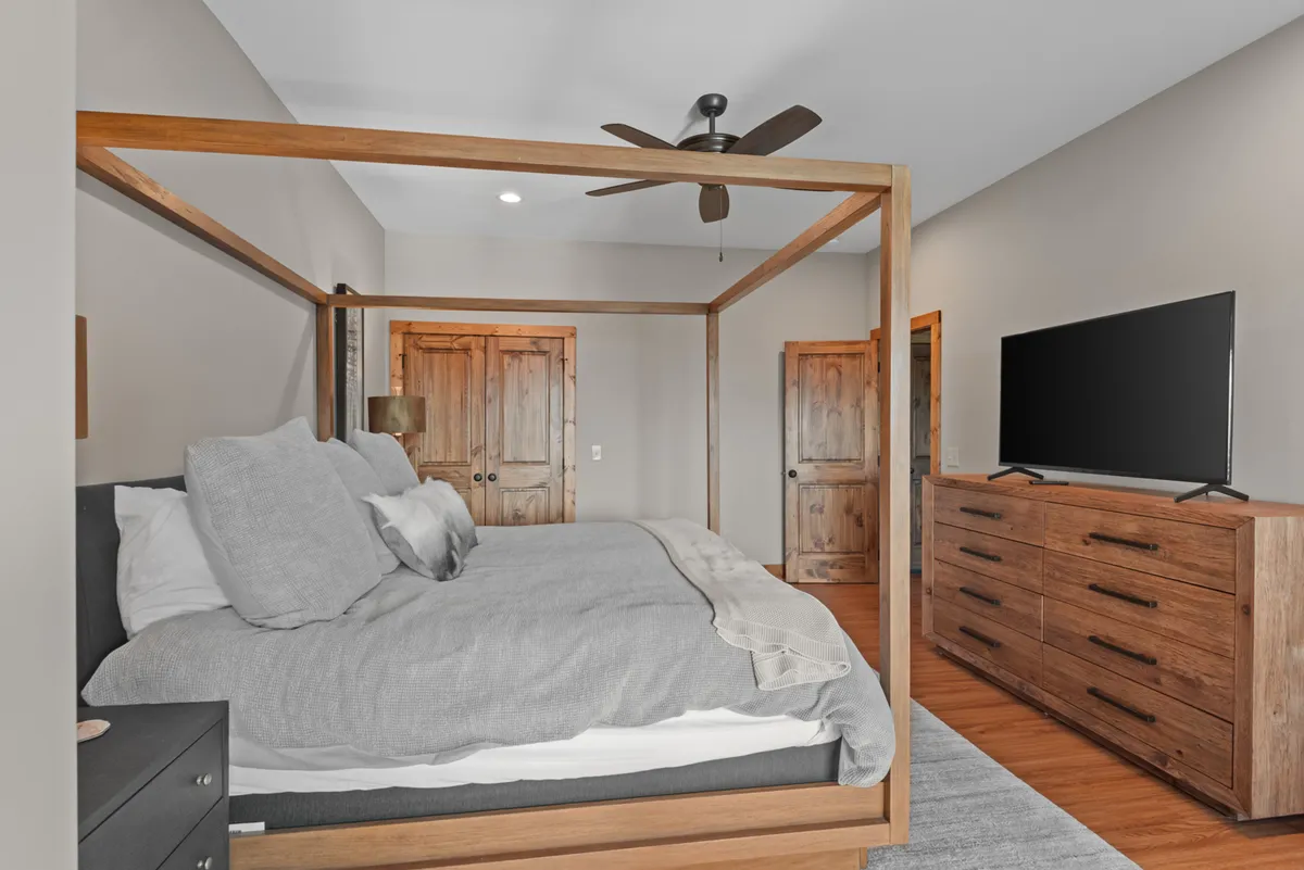 This image showcases a calm, cozy bedroom with a four-poster bed, a wooden dresser, a television, and wooden doors. The soft lighting and warm materials create a restful atmosphere, perfect for relaxing after a long day.