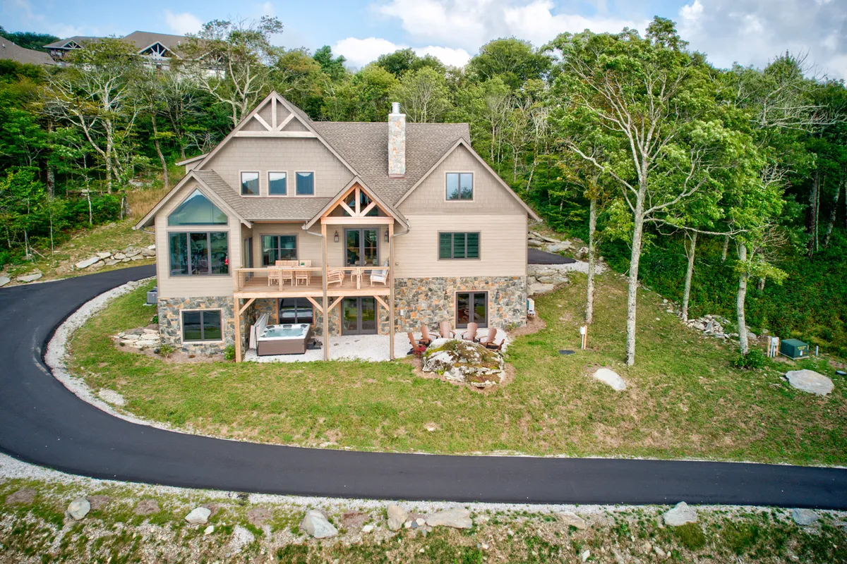 A welcoming exterior featuring a large stone and wood front porch, expansive windows, and a beautifully landscaped yard complete with a fire pit. The setting is ideal for relaxing after a day of adventure or gathering with friends and family outdoors.
