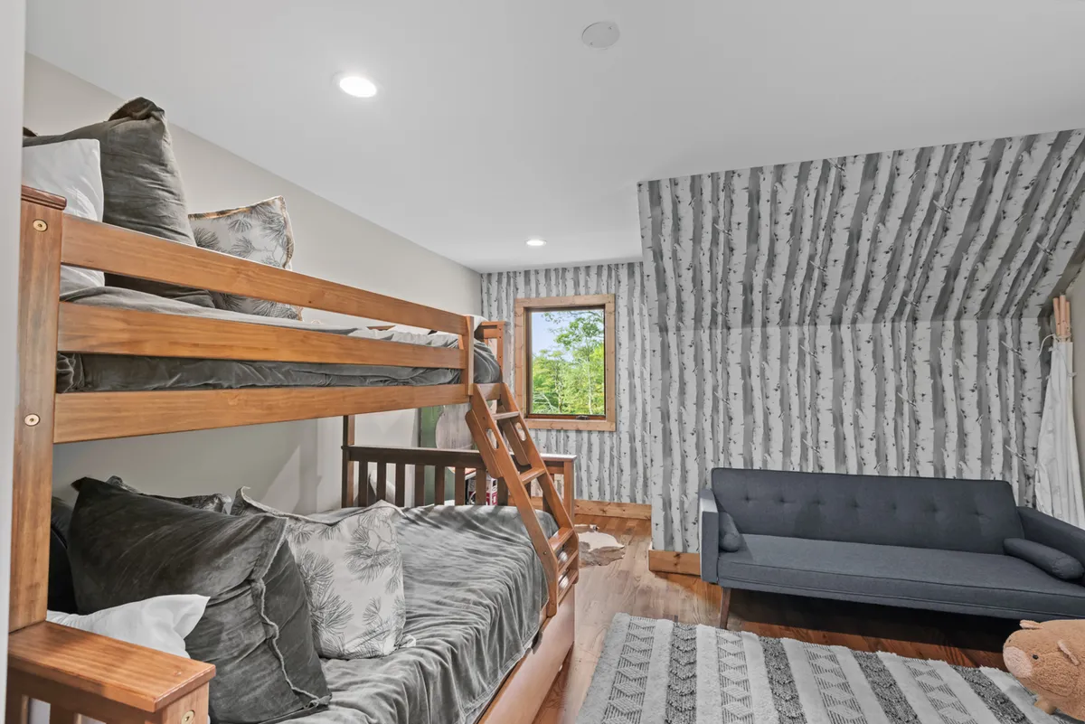 A playful and comfortable bunk room with bunk beds, a window view, a cozy sofa, and textured wallpaper. The room is brightly lit, inviting children to relax, play, or read together.