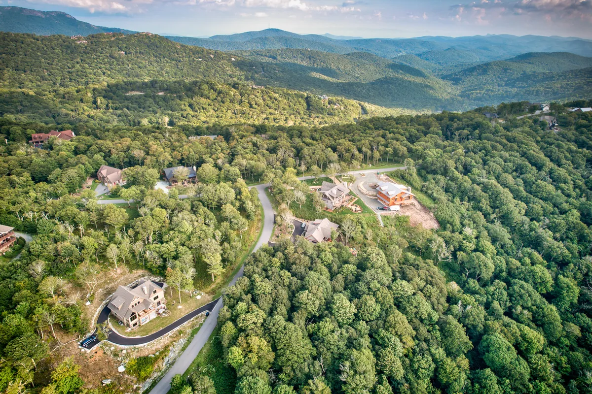A sweeping exterior shot capturing a sprawling forest, distant mountain ranges, and luxury homes dotting the landscape. The scene is serene and emphasizes natural beauty, adventure, and the inviting environment of the High Country.