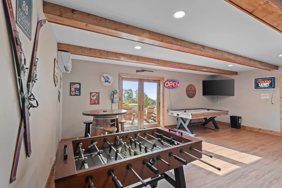 This image showcases a lively game room featuring a foosball table, pool table, and barrel-style table, with an open door leading to the outside. The space is styled for fun and relaxation, perfect for friendly competitions or casual hangouts.