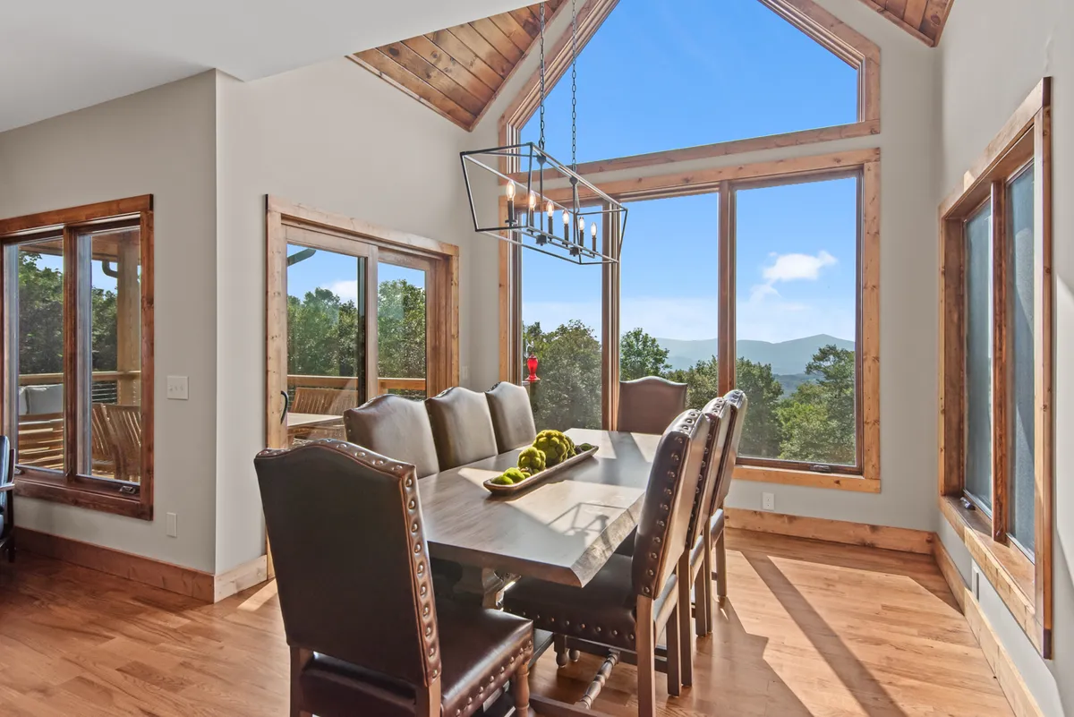 A dining area with a large table under a chandelier, surrounded by panoramic windows offering sweeping views. The space feels open and is perfect for family dinners or lively gatherings.
