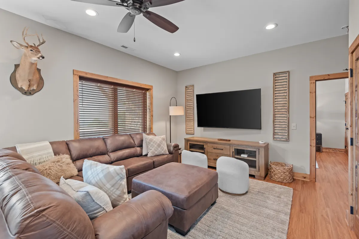 A cozy den is depicted with a leather sectional couch facing a large flat-screen TV, wooden entertainment center, and decorative touches like a mounted deer head. The ambiance is inviting, perfect for movie nights or quiet relaxation after games.
