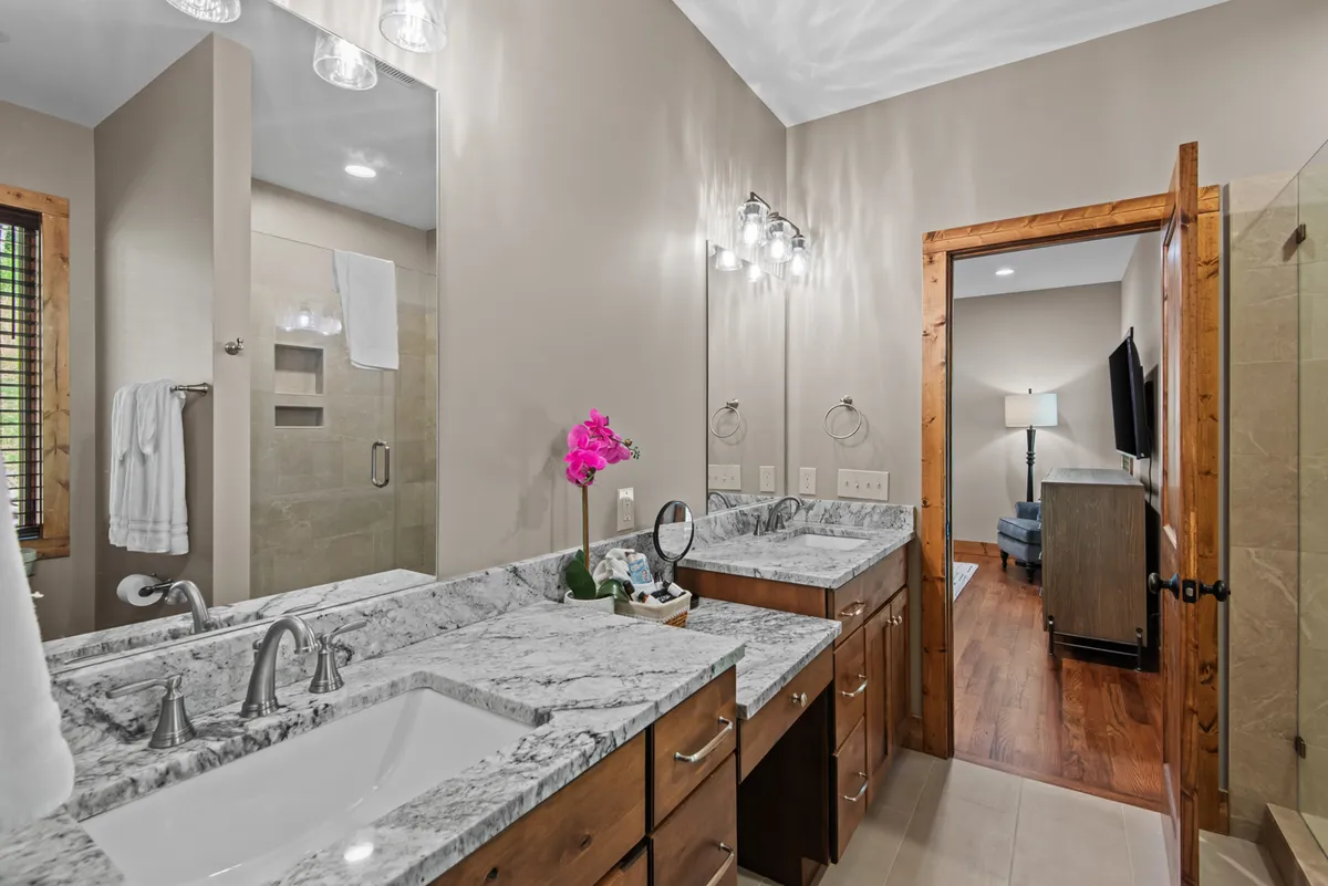 A sparkling bathroom with a double vanity topped by a marble countertop, pink orchid decoration, framed mirror, and a spacious glass shower enclosure. The space is bright, modern, and impeccably maintained.